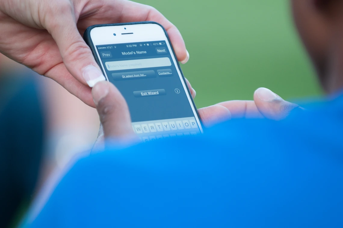 Close-up of a person using a smartphone app, with hands visible entering information on a form labeled “Model’s Name”