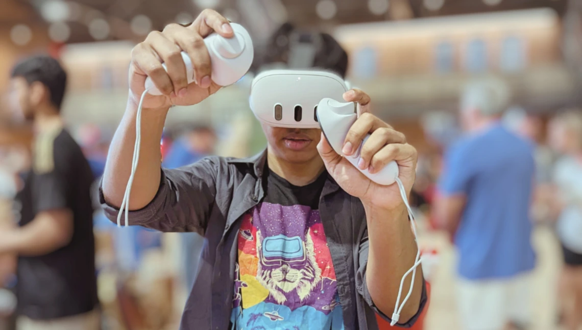 University of Arizona student using a virtual reality headset and controllers during an interactive AI event, wearing an “AI CORE” shirt